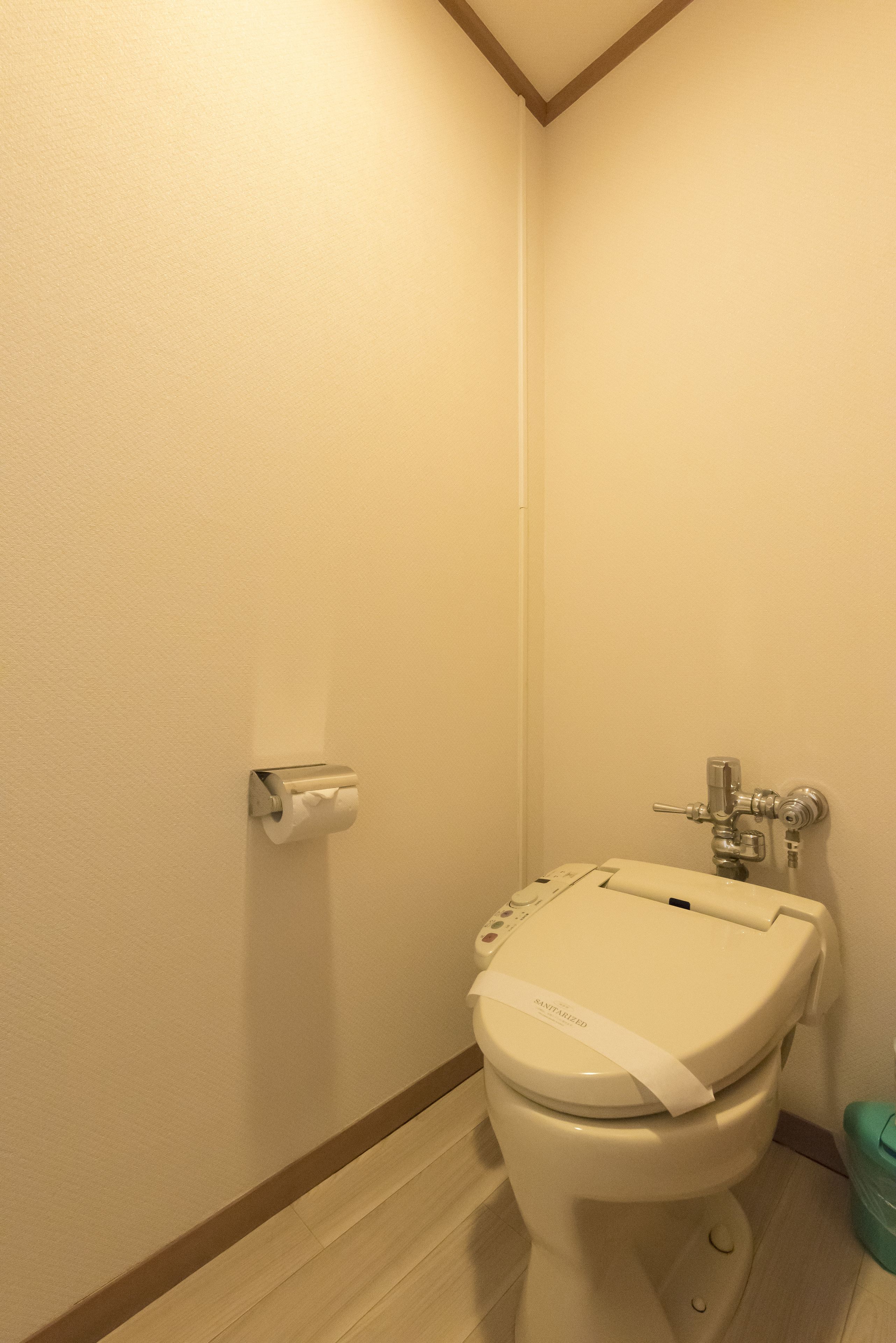 Een kleine, schone badkamer met toilet, papieren handdoekjes en een afvalbak.