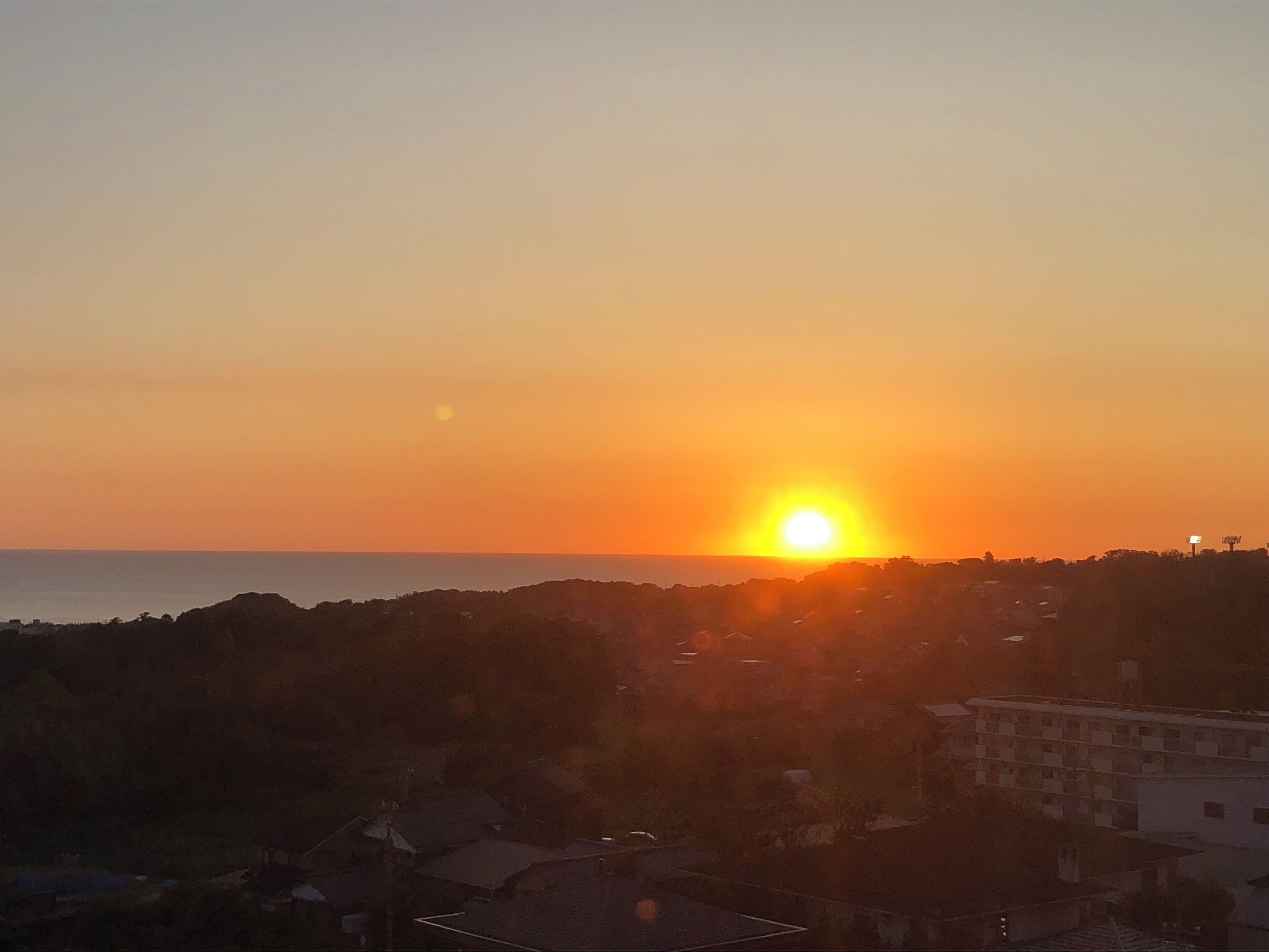 Tramonto su una costa con edifici e colline sullo sfondo.