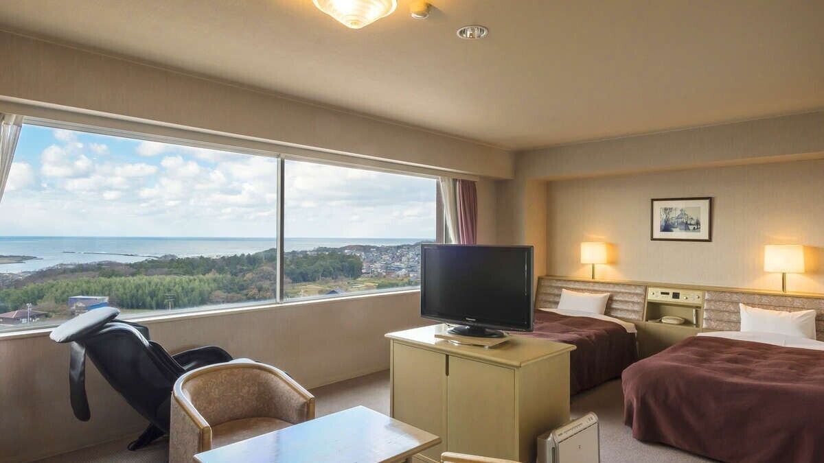 Ein Hotelzimmer mit großem Fenster, Fernseher, zwei Betten, Schreibtisch und Stuhl.