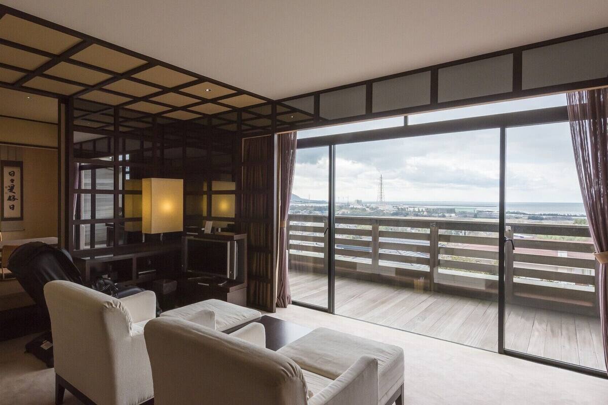 A hotel room with a balcony, a TV, a sofa, and a traditional Japanese decor.