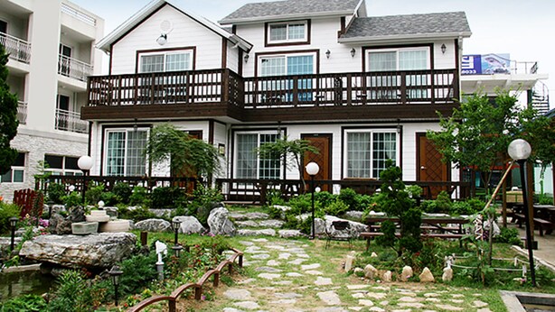 A two-story building with a balcony, stone pathway, and garden area.