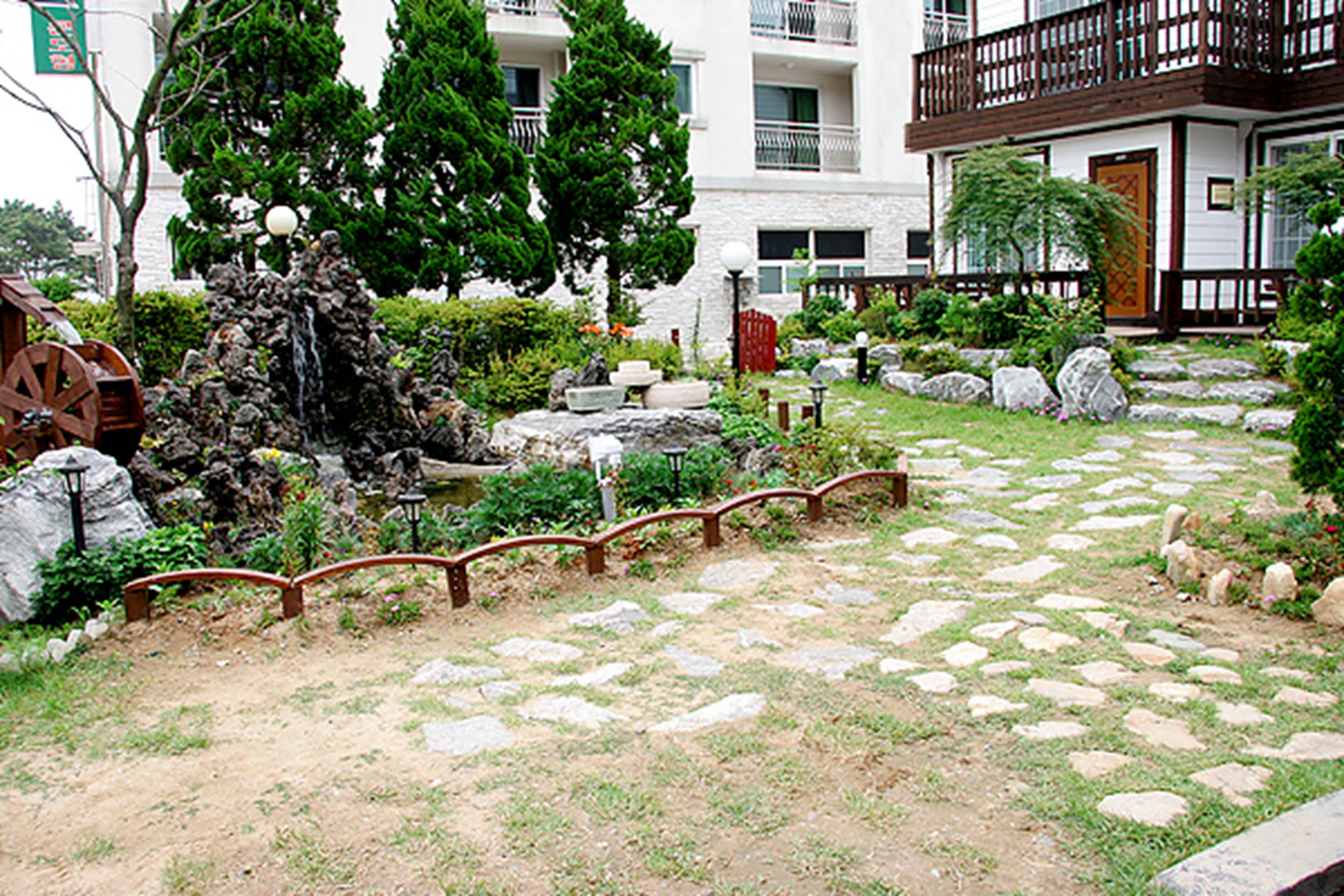 A garden pathway with stepping stones, a wooden fence, and a water feature.