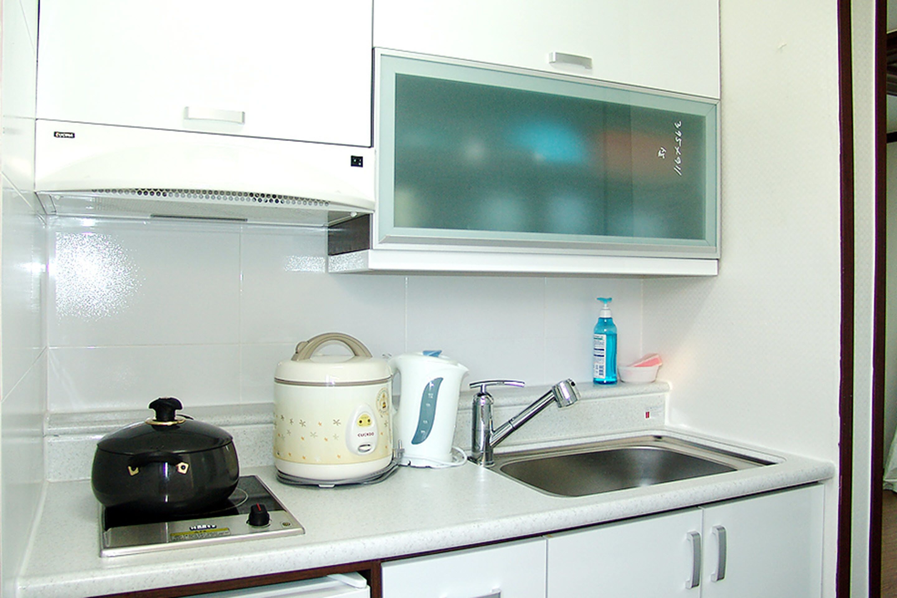 A kitchen with a stove, a rice cooker, a kettle, and a sink.