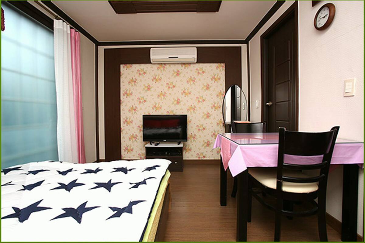 Une chambre d’hôtel équipée d’un lit, d’une télévision, d’un bureau avec une chaise et d’une horloge murale.