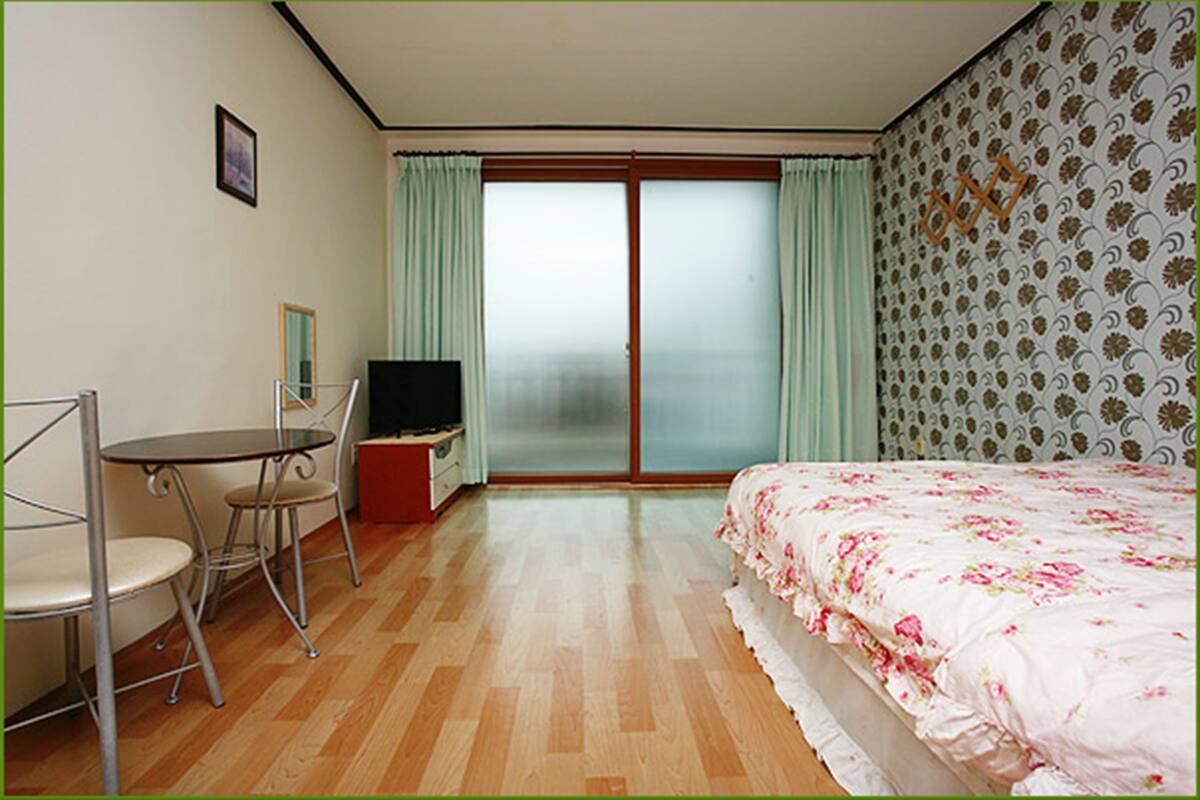 Une chambre d’hôtel avec un lit, une télévision, un bureau avec une chaise et une fenêtre avec des rideaux.