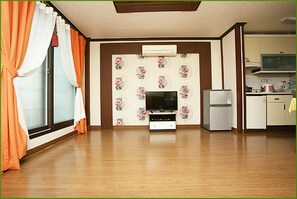 A living room with a flat-screen TV, a small refrigerator, and a kitchen area with cabinets and a microwave.