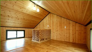 A spacious room with wooden walls and ceiling, a wooden floor, a window, and a lattice partition.