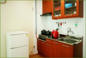 A compact kitchen with a white refrigerator, wooden cabinets, a gas stove, and a sink.