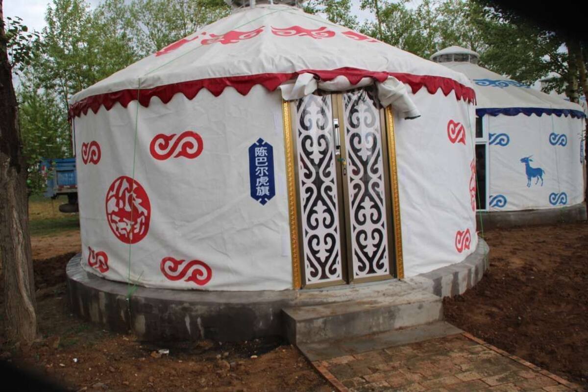 Uma yurt tradicional com exterior branco e vermelho, apresentando padrões pretos intrincados e uma porta central com moldura dourada.