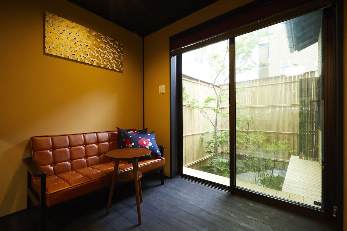 A room with a brown leather sofa, a small round table, and a large sliding glass door leading to a fenced outdoor area.