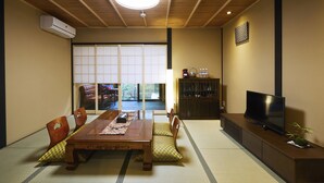 A traditional Japanese-style living room with tatami flooring, a wooden dining table, and a television on a cabinet.