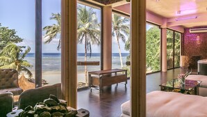 Una habitación con un gran ventanal con vista a la playa, una mesa de madera y un área de descanso.