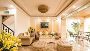 A spacious living area with a sofa set, ottomans, a coffee table, and a painting on the wall. - Sao Bang Hotel (Hanoi)