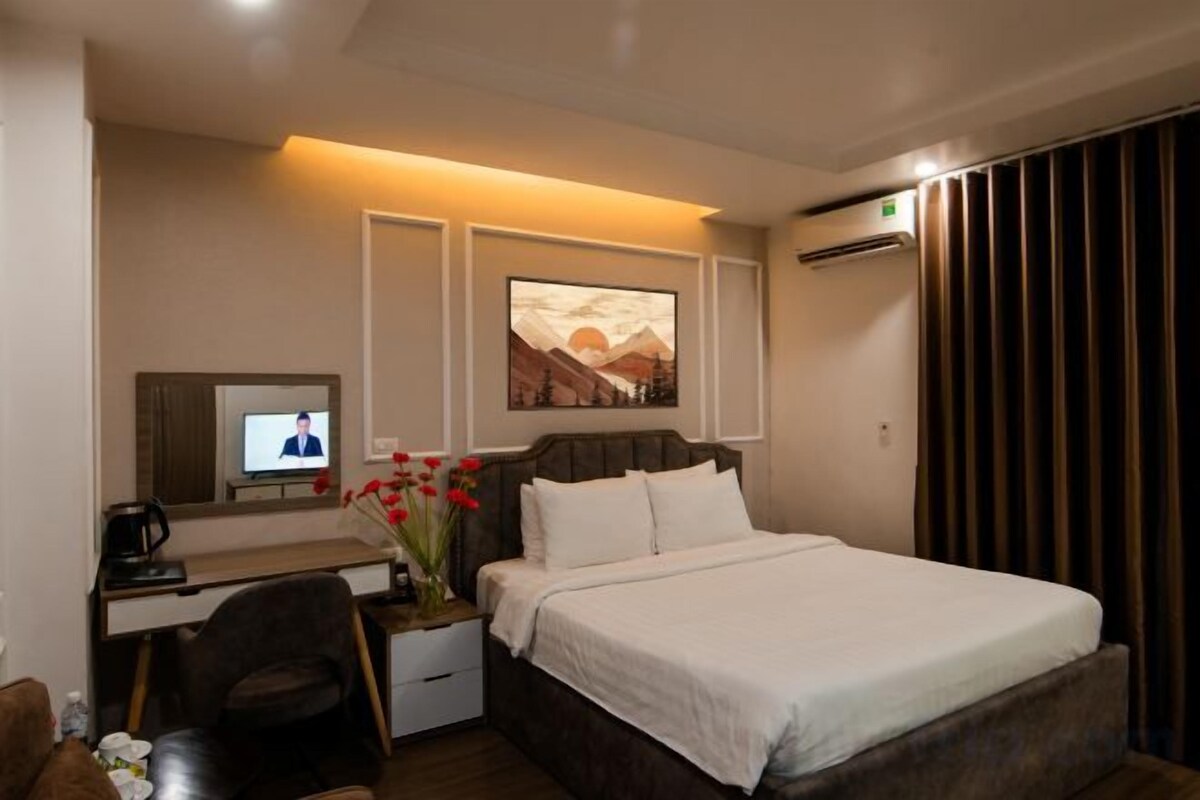 A hotel room with a bed, a desk with a computer, a TV, and a painting on the wall.