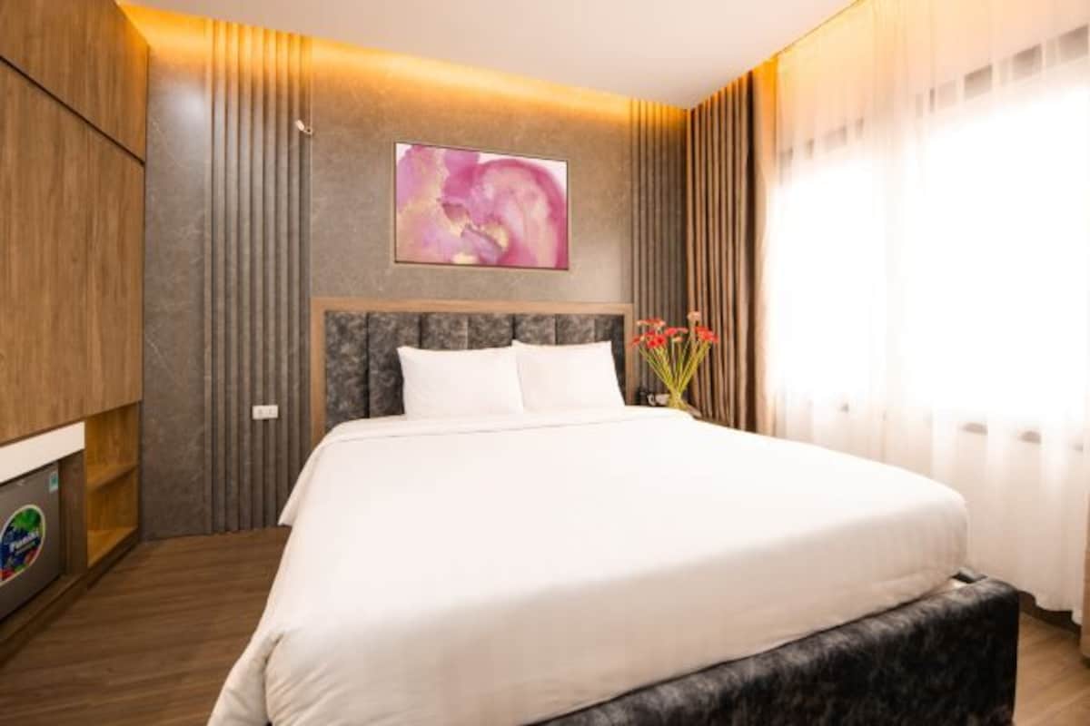 A modern hotel room with a large bed, a wooden wardrobe, and a wall-mounted artwork.