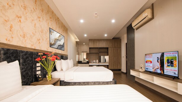 A hotel room with two beds, a small desk, a vase with flowers, and a TV on the wall. - Sao Bang Hotel (Hanoi)