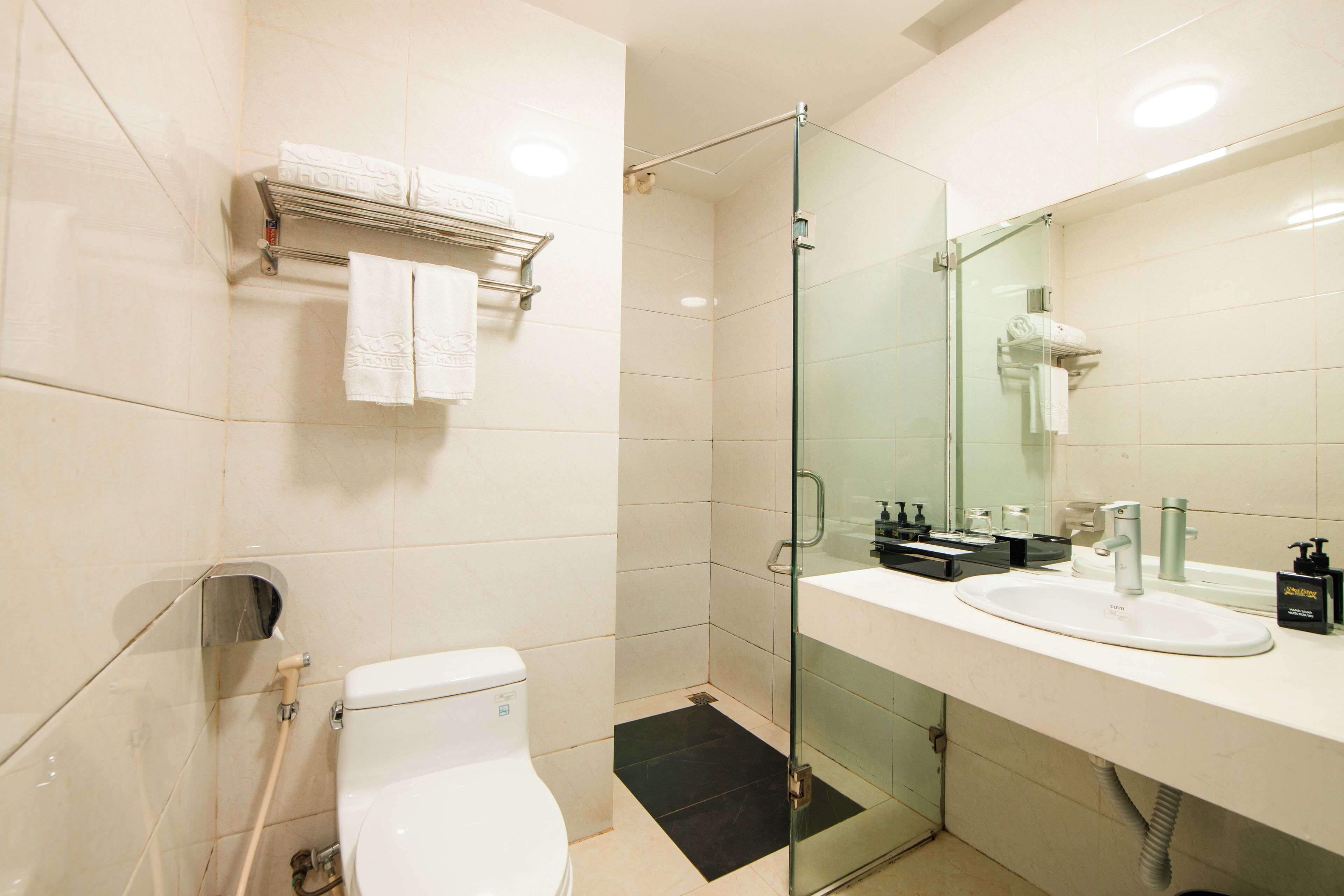 Et moderne badeværelse med et glasafskærmet brusebad, et hvidt toilet, en vask med et spejl og en håndklæderække.