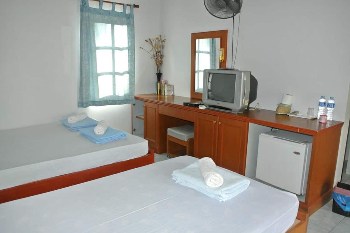 A room with a bed, a desk with a television, a small refrigerator, and a window with a curtain.