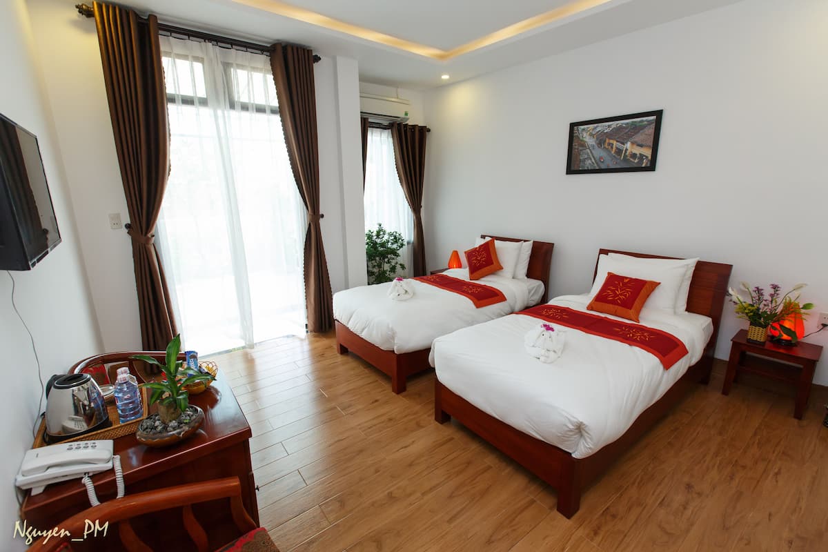 A hotel room with two beds, a desk with a telephone and a coffee maker, and a small table with a plant and a basket.