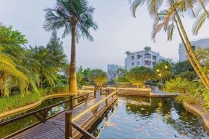 Un puente de madera sobre el agua, rodeado de palmeras y vegetación, con un edificio al fondo.