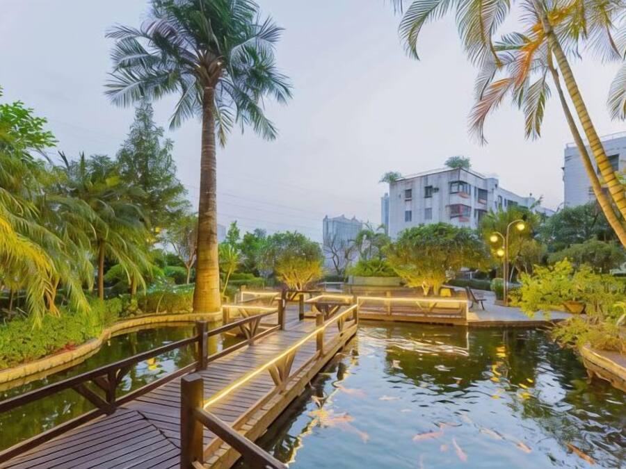 A wooden bridge over a water body with palm trees and a building in the background.