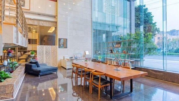 A modern hotel lobby with a wooden dining table, chairs, a sofa, and a staircase. - Delight Empire Hotel (Dongguan)