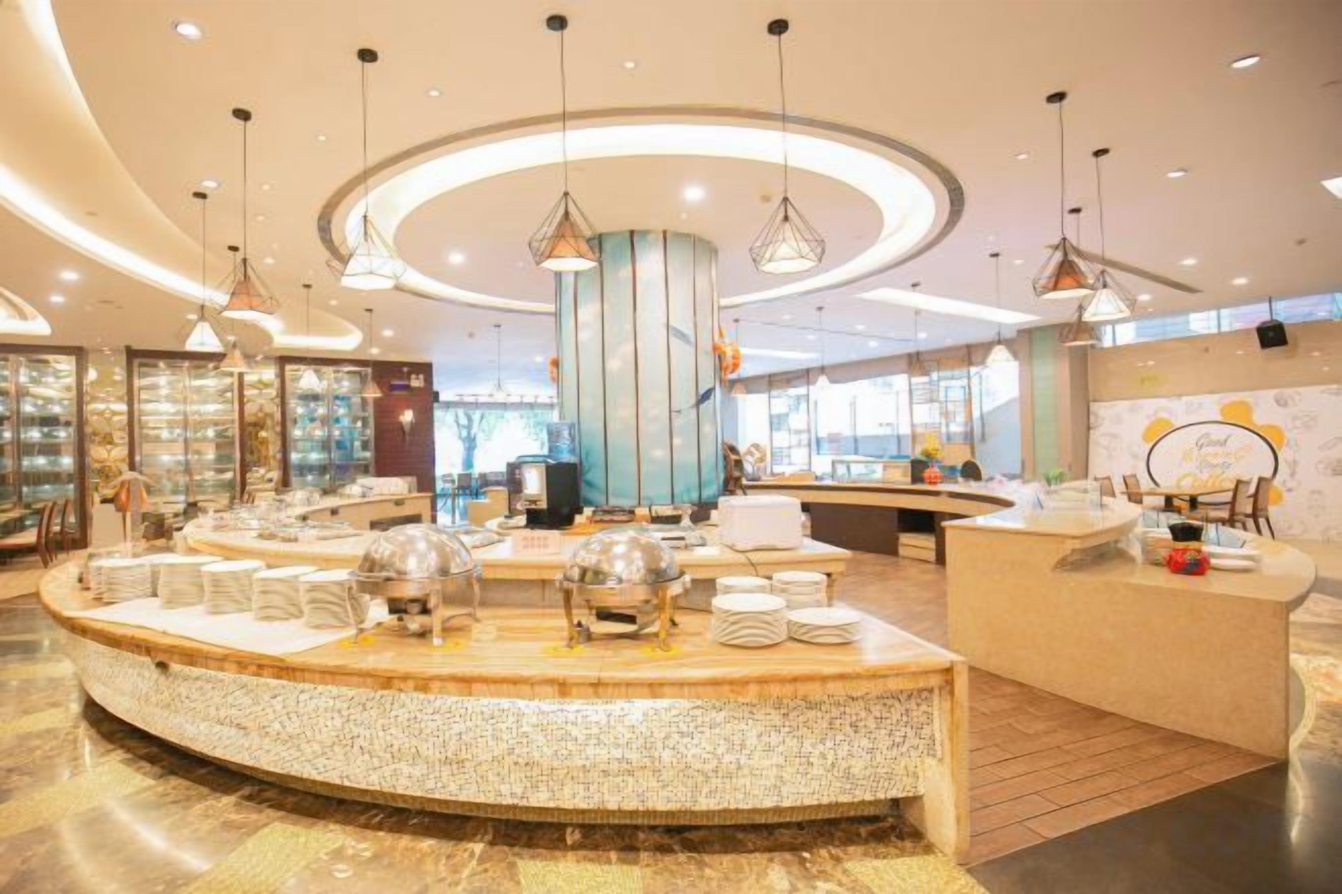 Un hall d’hôtel moderne avec un comptoir d’accueil central, un espace salon circulaire et des luminaires suspendus.