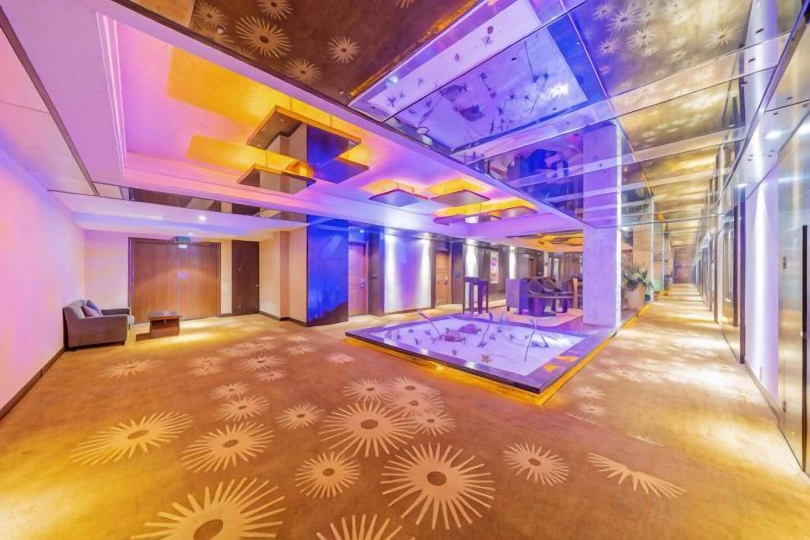 A hotel lobby with a central ice rink, seating areas, and a modern ceiling design.