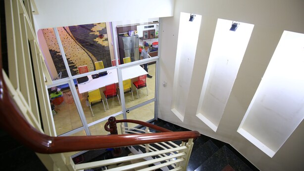 A staircase with a wooden handrail leading to a room with a large window. - My Homestay - Hostel (Nha Trang)