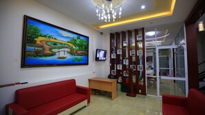 A hotel lobby with a red sofa, a wooden desk, a large painting, a chandelier, and a glass door leading to a balcony. - My Homestay - Hostel (Nha Trang)