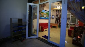 A room with a glass door leading to a living area, a red sofa, a bookshelf, and a painting on the wall. - My Homestay - Hostel (Nha Trang)
