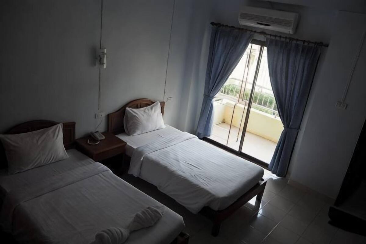 Habitación de hotel con dos camas, una mesita de noche y una ventana con cortinas.