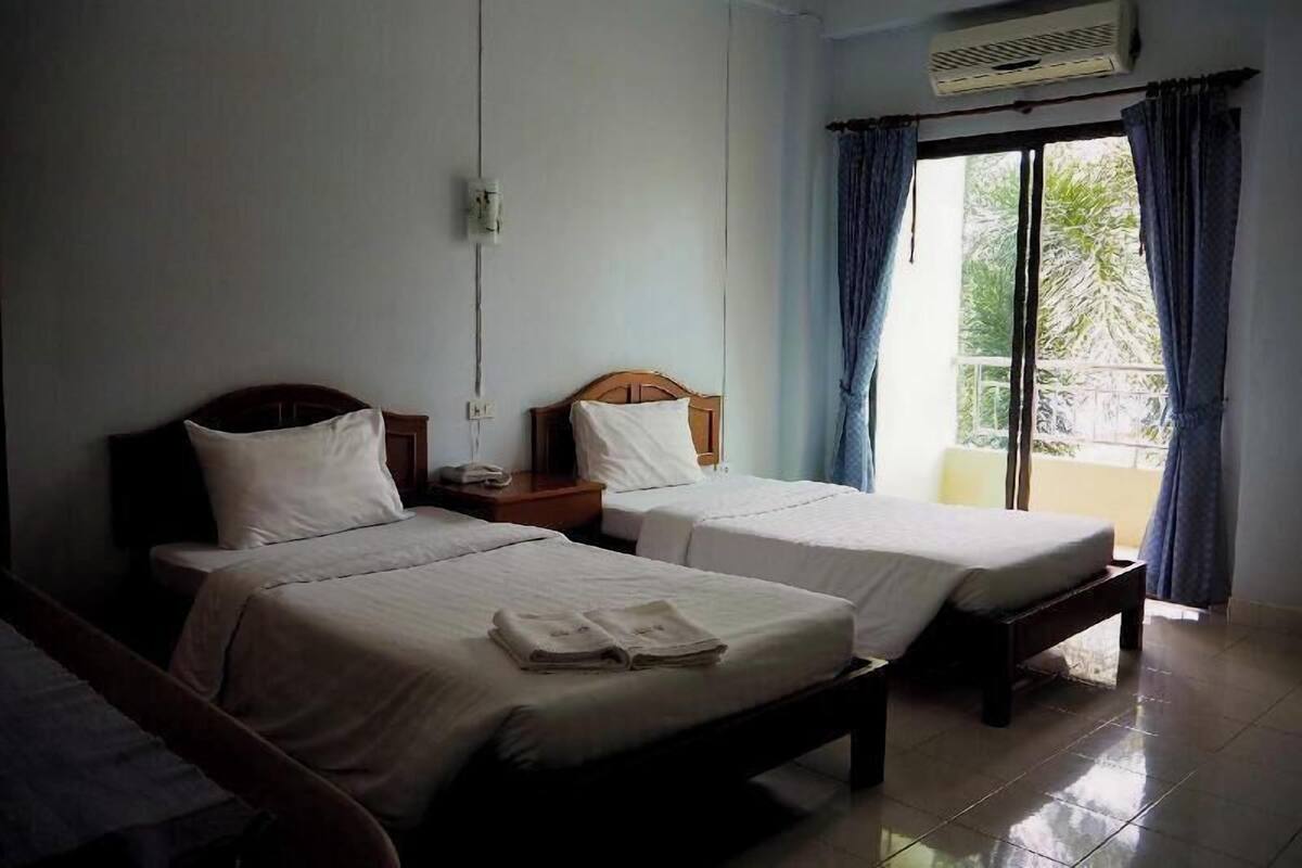 Una habitación de hotel con dos camas individuales, una mesita de noche, un enchufe y una ventana con cortinas.