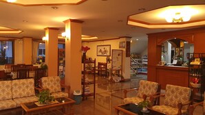 A hotel lobby with a reception desk, seating area with patterned sofas and armchairs, a coffee table, and a large mirror reflecting the interior. - Ritzy House Hotel (Chumphon)