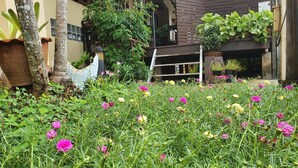 A garden with various plants and flowers, a wooden structure, and a building in the background. - Ritzy House Hotel (Chumphon)