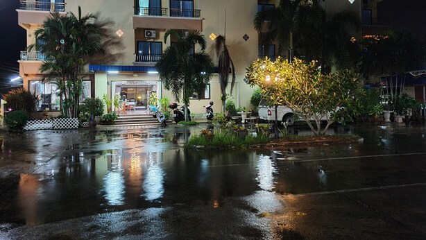 A multi-story hotel with balconies, a central entrance, and a reflective wet ground. - Ritzy House Hotel (Chumphon)