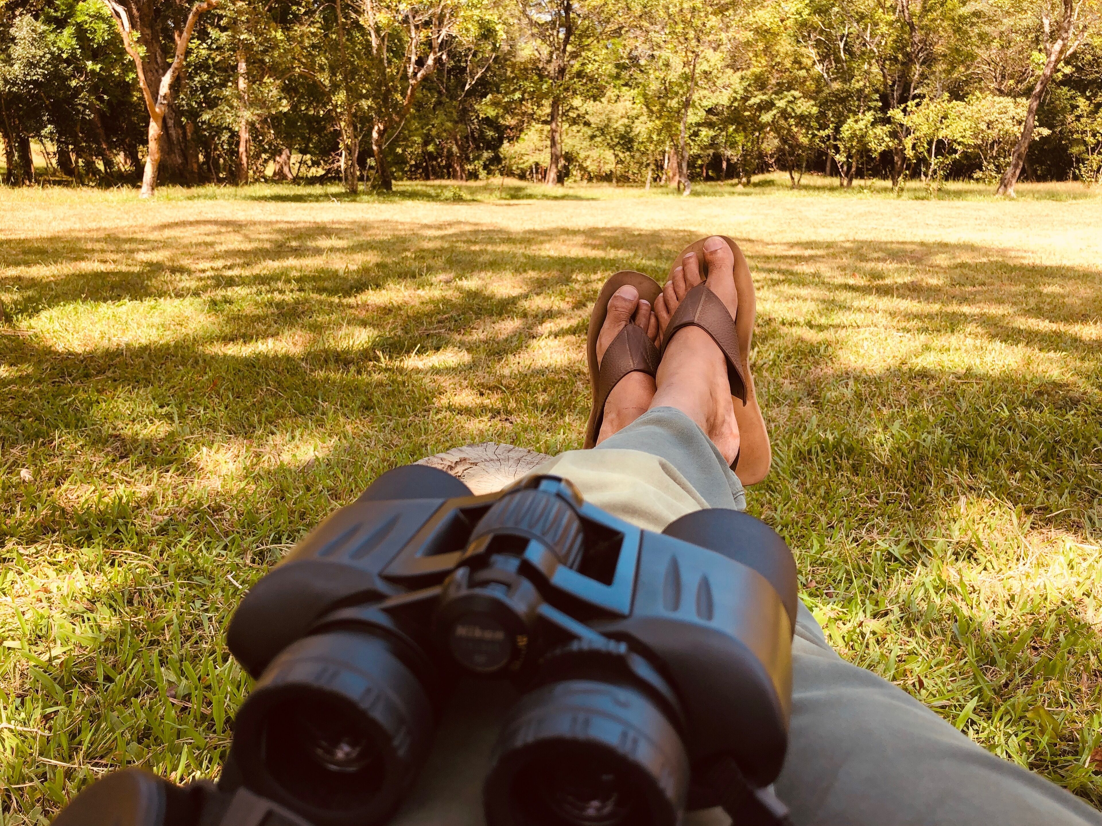 A person's legs and feet resting on grass with binoculars in front.