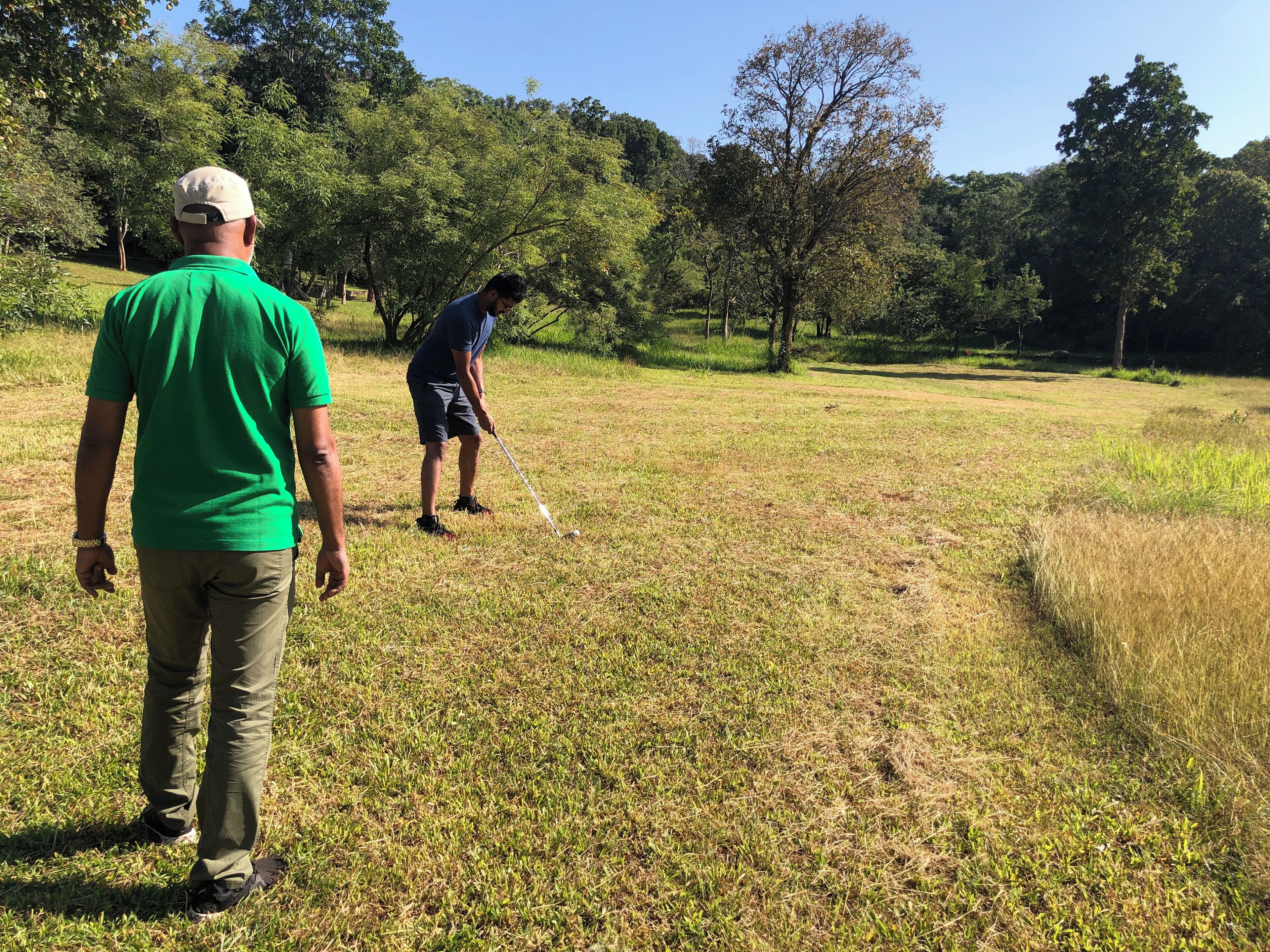 A grassy field with two people, one standing and one bending over, possibly playing golf.