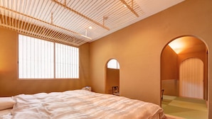 A bedroom with a large bed, a window with blinds, an arched doorway, and a wooden floor. - Shouen (Izumo)