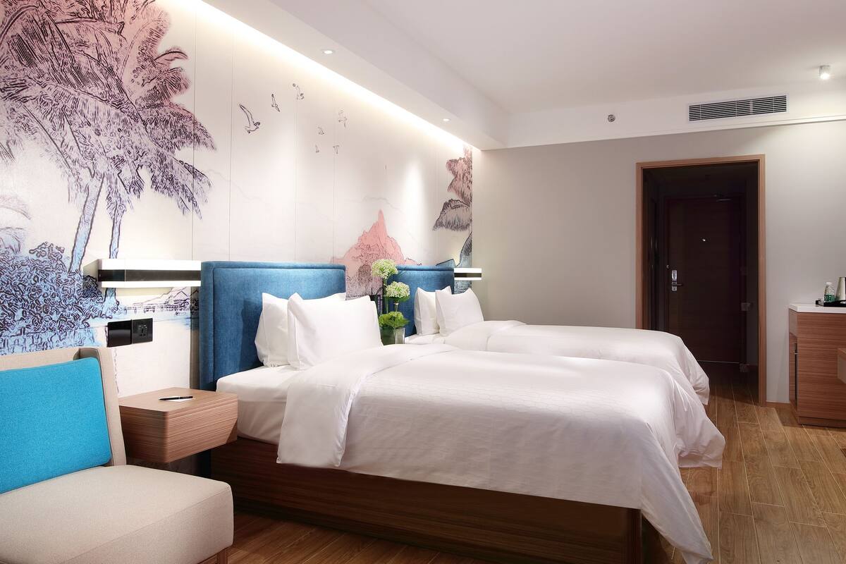 A modern hotel room with a large bed, a seating area, a TV, and a wall mural.