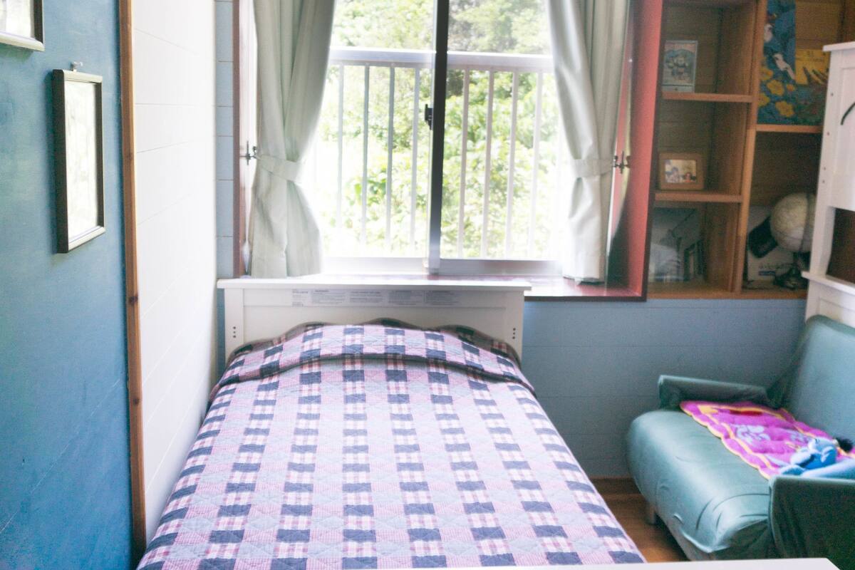 A bedroom with a bed, a window with curtains, a chair, and a bookshelf.