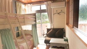 A cozy room with bunk beds, a small sofa, a table, and a window with a view of greenery. - Amakara Okinawa (Nago)