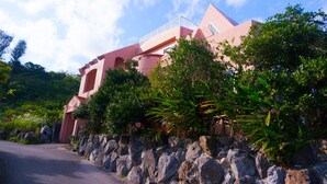 A pink building with a balcony, surrounded by greenery and rocks. - Amakara Okinawa (Nago)