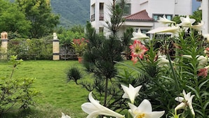 A modern two-story building with a white exterior and red-tiled roof, surrounded by lush greenery and flowering plants. - Slow Fly B&B (Xincheng)