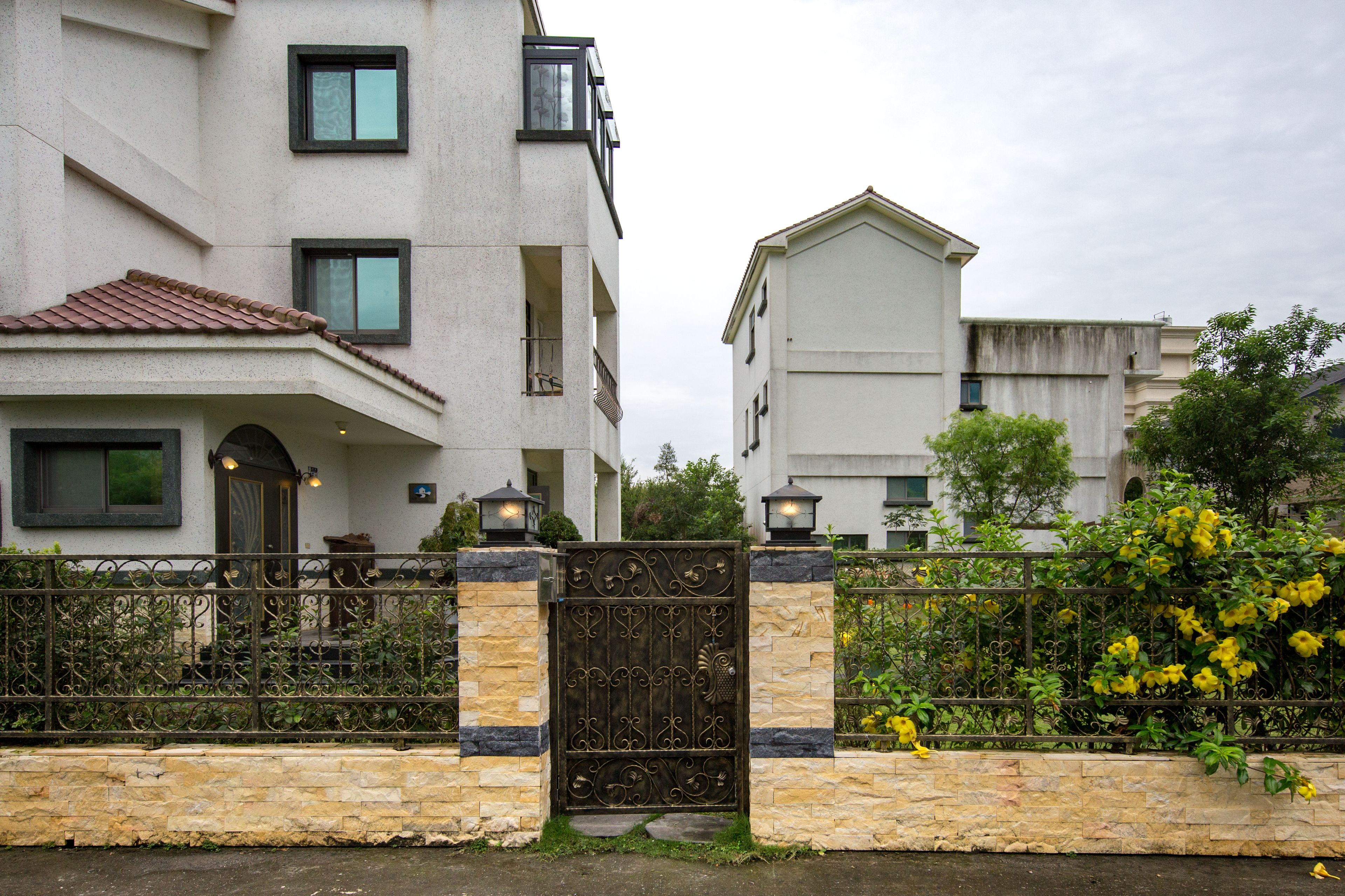 A gated residential area with a stone wall and metal gate, flanked by two-story buildings with balconies and windows.