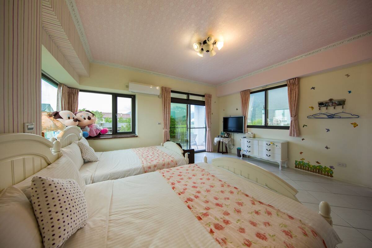 Un dormitorio con dos camas, televisión, cómoda y ventana con cortinas.