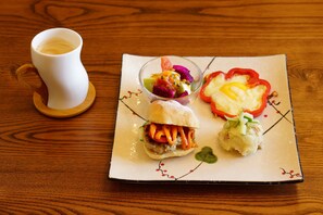 A square plate with a sandwich, a fruit salad, and a vegetable dish on a wooden table.
