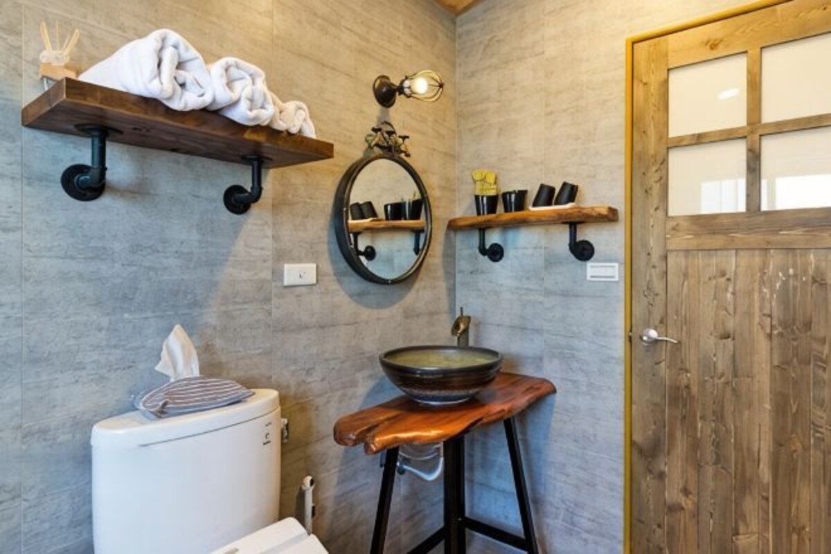 A bathroom with a toilet, sink, mirror, and wooden door.