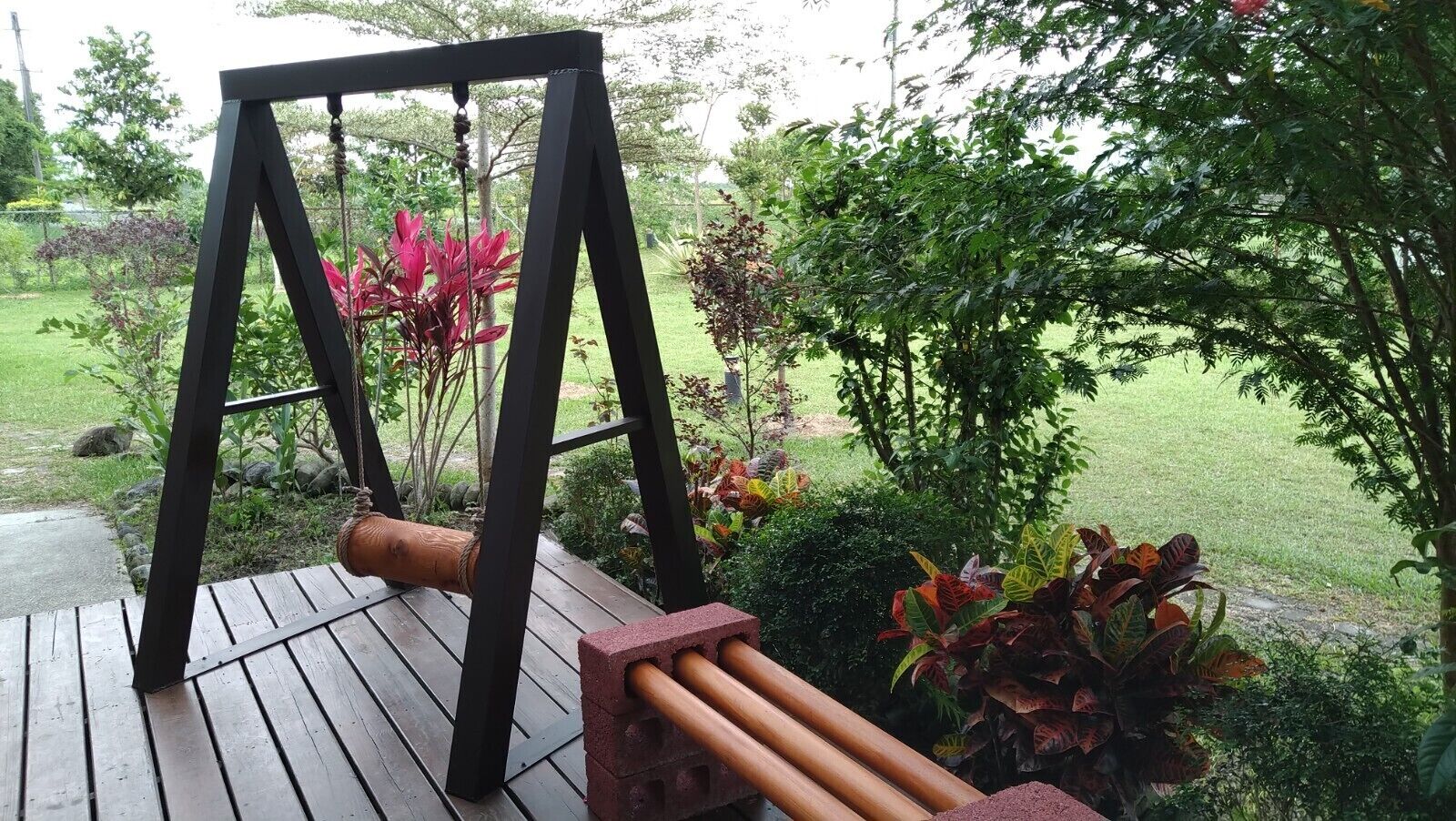 Une terrasse en bois avec une balançoire et un jardin en briques muni d’un tuyau.