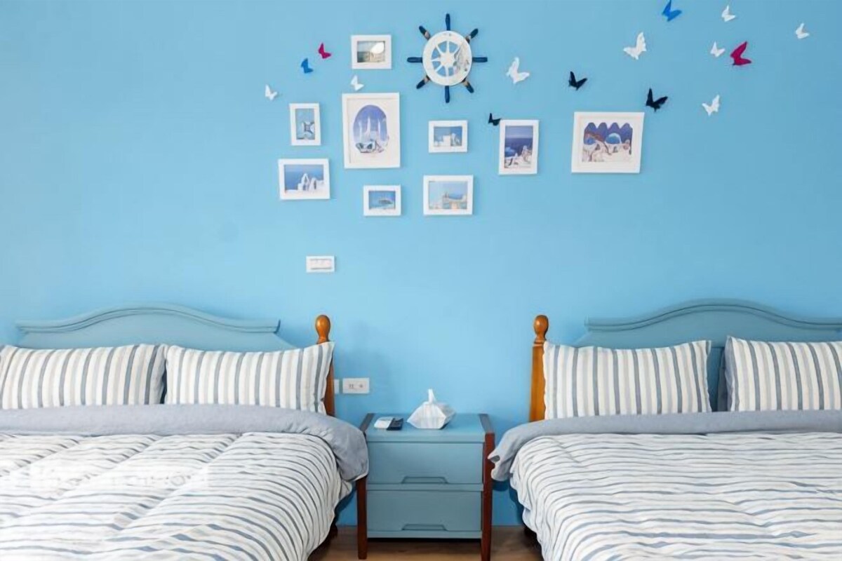 A bedroom with two beds, a nightstand, and a wall decorated with pictures and butterflies.